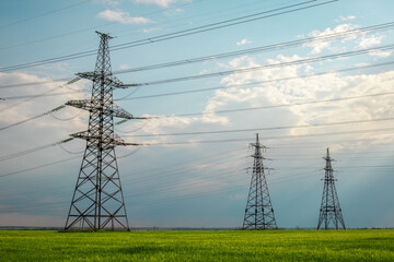 High voltage lines and power pylons in a flat and green agricultural landscape on a sunny day with...
