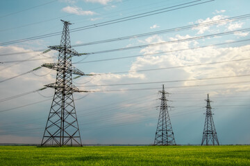 High voltage lines and power pylons in a flat and green agricultural landscape on a sunny day with clouds in the blue sky. Cloudy and rainy. Wheat is growing