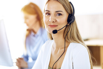 Portrait of call center operator at work in sunny office. Group of people in a headset ready to...