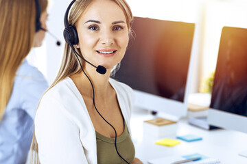 Portrait of call center operator at work in sunny office. Group of people in a headset ready to help customers. Business concept