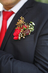 The groom's wedding boutonniere of succulents and red flowers in a black jacket with a red tie. Festive decor, flowers, attire for the marriage registration. Close-up, space for text