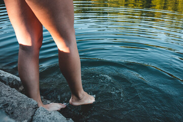 Young woman tests water before entering for a swim. Legs close-up
