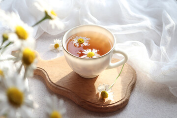 Chamomile tea in a white Cup on a wooden Board on a background of a delicate white napkin, close-up, side view, bokeh