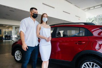 Fototapeta na wymiar Young couple in masks selects a new vehicle and consult with a representative of the dealership in the period of the pandemic. Car sales, and life during the pandemic