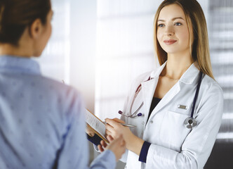 Young woman-doctor and her patient are discussing patient's current health examination, while...