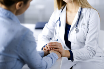 Unknown woman-doctor is holding her patient's hands to reassure the patient, discussing current...