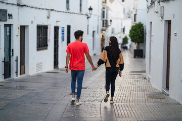 Pareja joven cogida de la manos caminando por pueblo blanco