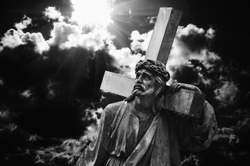 Jesus Christ with cross against dramatic view of cloudy sky.  Ancient statue.