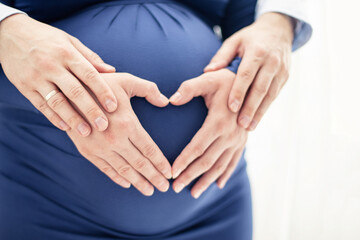 Man's hands touch pregnant woman's heart-shaped hands on her baby bump. Bright photo on white background