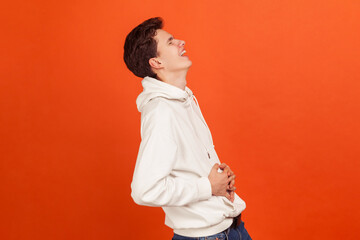 Profile portrait of teenager in hoodie holding his belly and laughing out loud. Funny story, good...