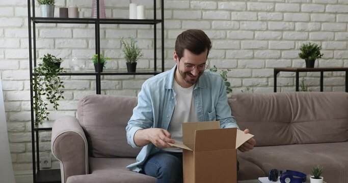 Man sit on couch opening carton parcel box feels satisfied by goods delivered from on-line webshop store. E-shopping e-commerce buyer, trusted transporting company fragile items are in order concept