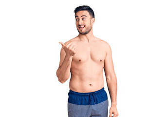 Fototapeta premium Young handsome man wearing swimwear smiling with happy face looking and pointing to the side with thumb up.