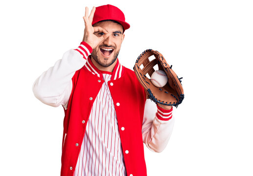 Young handsome man holding baseball gloves smiling happy doing ok sign with hand on eye looking through fingers