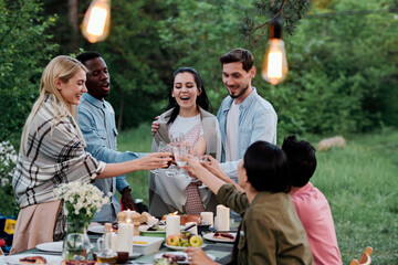 Three happy young restful couples sitting by served table in natural environment