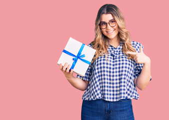 Young caucasian woman holding gift pointing finger to one self smiling happy and proud