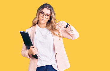 Young caucasian woman wearing business clothes and glasses holding binder with angry face, negative...