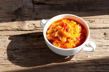 Delicious juicy appetizer of stewed vegetables in white bowl on  old wooden table. Rustic style. Sunlight and sharp shadows. Selective focus