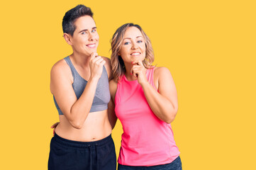 Fototapeta na wymiar Couple of women wearing sportswear looking confident at the camera smiling with crossed arms and hand raised on chin. thinking positive.
