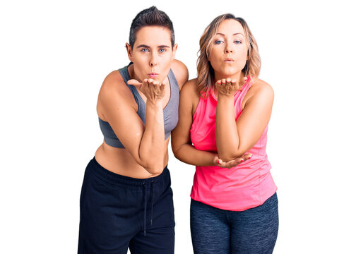 Couple of women wearing sportswear looking at the camera blowing a kiss with hand on air being lovely and sexy. love expression.