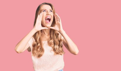 Young beautiful caucasian woman with blond hair wearing casual clothes shouting angry out loud with hands over mouth