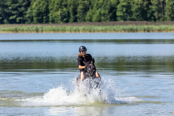 Fototapeta na wymiar Horseback riding teenager girl galloping throug the water