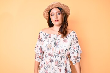 Young beautiful caucasian woman wearing summer dress and hat relaxed with serious expression on face. simple and natural looking at the camera.