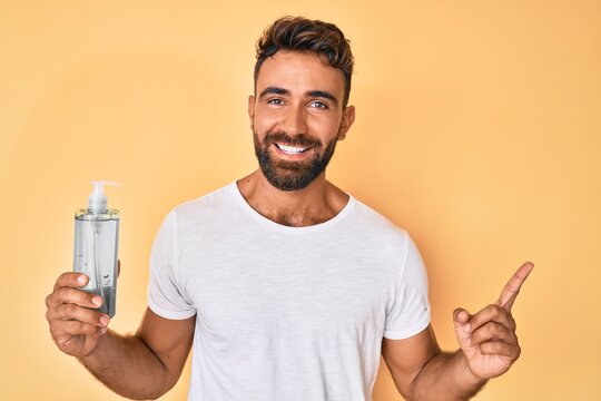 Young hispanic man using hand sanitizer gel smiling happy pointing with hand and finger to the side