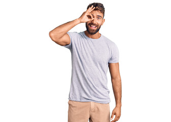 Young hispanic man wearing casual clothes doing ok gesture with hand smiling, eye looking through fingers with happy face.