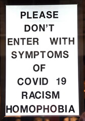 Schild in einem Schaufenster: "Don't enter with Symptoms of  Covid 19, Racism, Homophobia"  