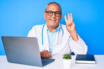 Senior handsome man with gray hair wearing doctor uniform working using computer laptop showing and pointing up with fingers number three while smiling confident and happy.