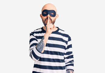 Young handsome man wearing burglar mask asking to be quiet with finger on lips. silence and secret concept.