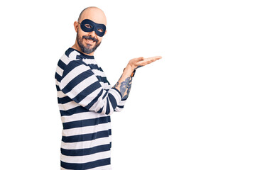Young handsome man wearing burglar mask pointing aside with hands open palms showing copy space, presenting advertisement smiling excited happy