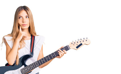 Fototapeta premium Beautiful caucasian woman with blonde hair playing electric guitar serious face thinking about question with hand on chin, thoughtful about confusing idea