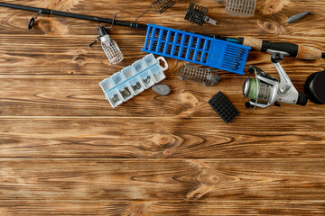 flat lay with fishing tackle, fishing rod and plastic box with fishing tackle and hooks, feeders on wooden planks, copy space