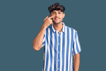 Naklejka premium Young hispanic man wearing casual clothes pointing with hand finger to face and nose, smiling cheerful. beauty concept