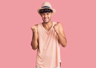 Young hispanic man wearing summer hat very happy and excited doing winner gesture with arms raised, smiling and screaming for success. celebration concept.