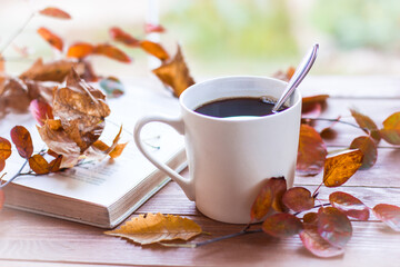 Autumn, autumn leaves, a hot steaming Cup of coffee and an old book and a grey scarf on the background of a wooden table. Seasonal, morning coffee, Sunday relaxation and still life concept.