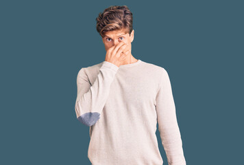 Young handsome man wearing casual clothes smelling something stinky and disgusting, intolerable...