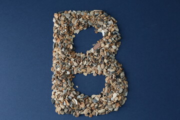 The letter B is lined with small pebbles on a blue background