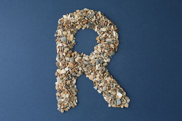 The letter R is lined with small pebbles on a blue background