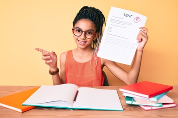 Young african american girl child with braids showing failed exam smiling happy pointing with hand and finger to the side