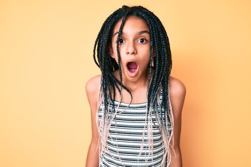 Young african american girl child with braids over yellow background scared and amazed with open...