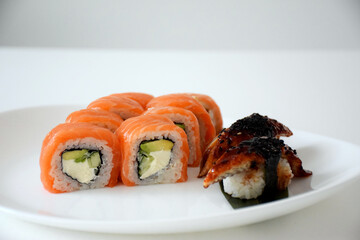 Set of Philadelphia sushi rolls with salmon, avocado, cheese and sashimi with eel and rice served on white plate. Traditional Japanese food.
