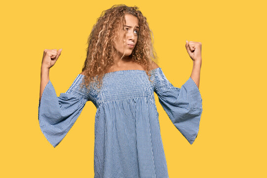 Beautiful caucasian teenager girl wearing summer dress showing arms muscles smiling proud. fitness concept.