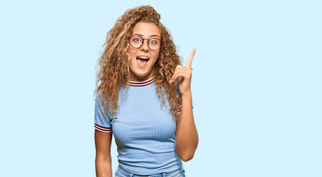 Beautiful caucasian teenager girl wearing casual clothes and glasses pointing finger up with successful idea. exited and happy. number one.