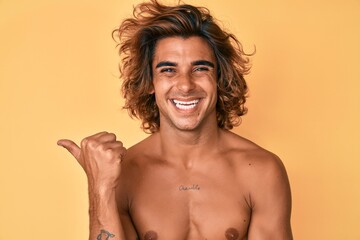 Young hispanic man standing shirtless smiling happy pointing with hand and finger to the side