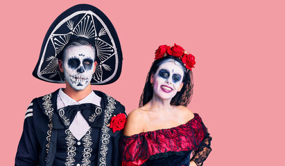 Young couple wearing mexican day of the dead costume over background winking looking at the camera with sexy expression, cheerful and happy face.