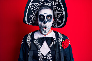 Young man wearing mexican day of the dead costume over red afraid and shocked with surprise expression, fear and excited face.