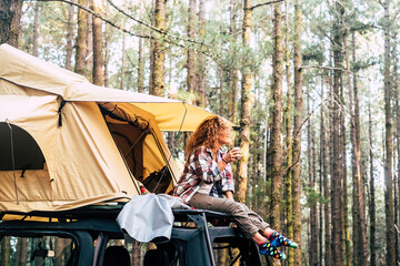 Concept of independence, freedom and travel with lonely woman sit down on the roof of the car outside the roof tent - beautiful nature and forest view outdoor © simona
