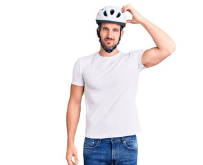 Young handsome man wearing bike helmet confuse and wonder about question. uncertain with doubt, thinking with hand on head. pensive concept.